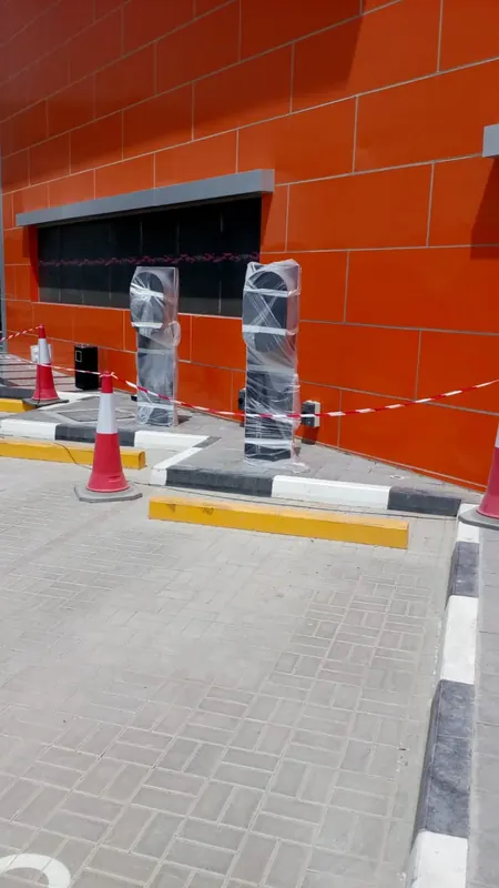 Two EV charger units wrapped in protective film beside a paved bay with kerb and yellow bay stop at Aloft Hotel