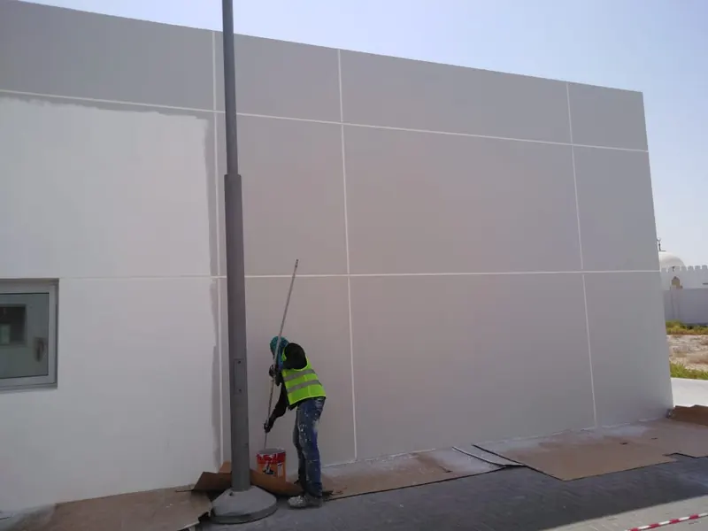 Painter repainting grey panelised external wall at Porsche service centre Sharjah